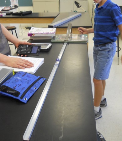 A marble moves along a track as students measure its velocity.