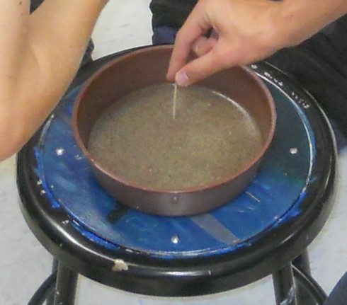 A bowl of water with black pepper floating on top, just before dipping in the soap covered toothpick.