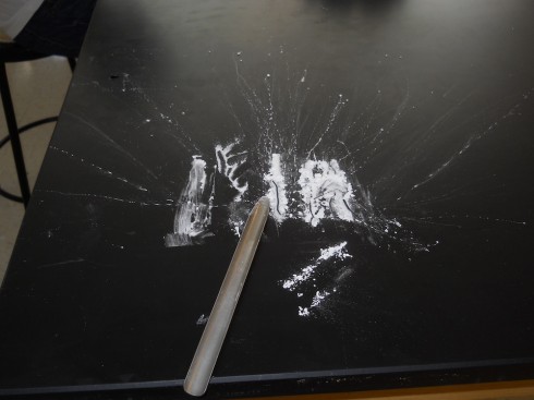The lines of powdered substance (cocaine) were severely disrupted by student's sampling, but you can still see the two full lines to the right and the half line that the spatula is touching. 