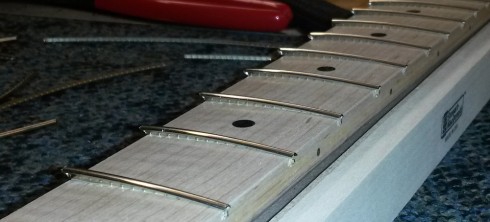 Placing the fret wire into the fret cuts. The wire still needs to be fully pressed in.