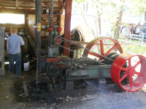 The steam engine. The rate at which it spins is controlled by a centrifugal governor (the red balls), which is quite an elegant device. The engine turns the large red wheels which are connected to the blade via a long belt.